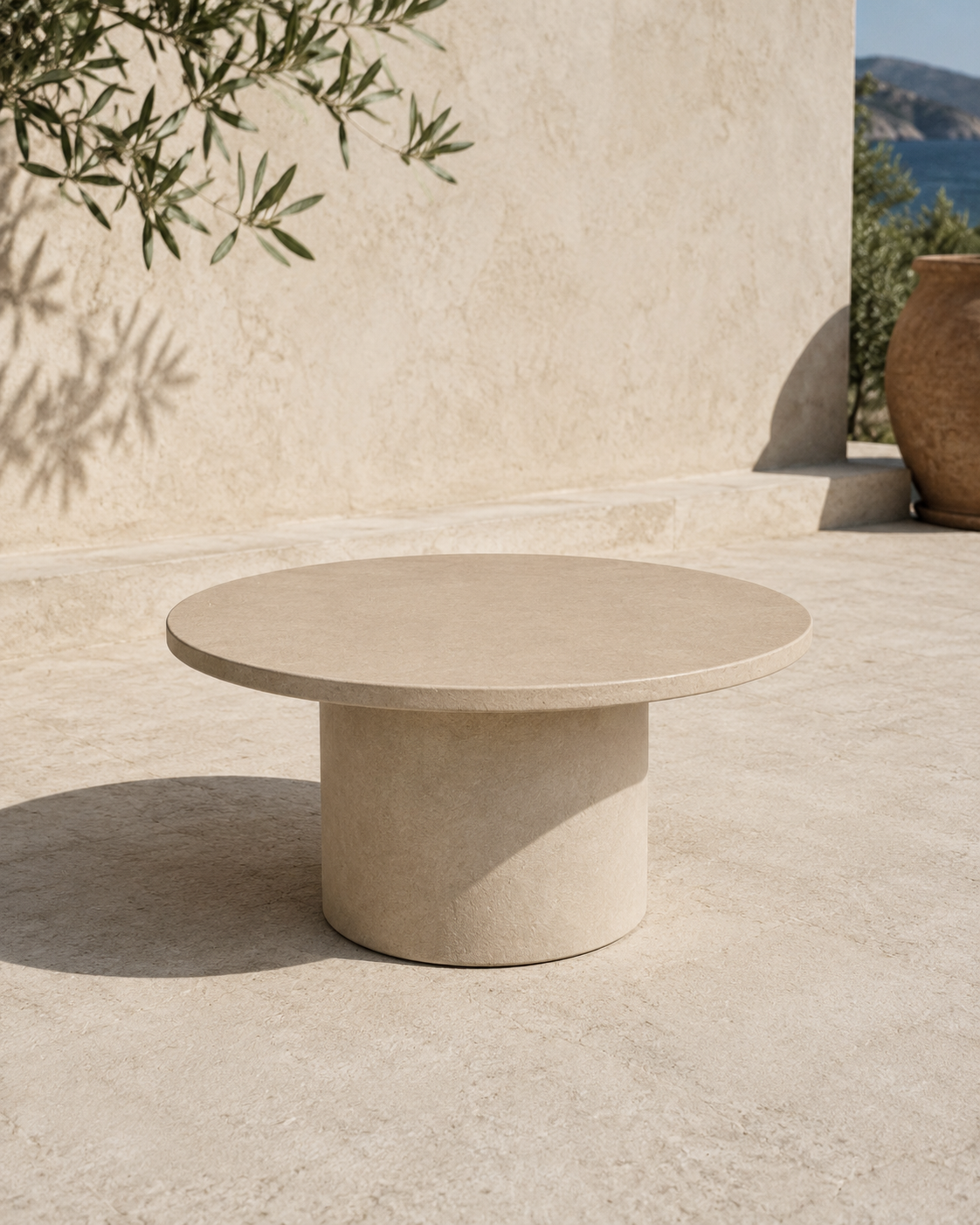 Tavolino ARKÉ MANOFATTI in finitura sabbia ambientato su una terrazza mediterranea in pietra con vista mare