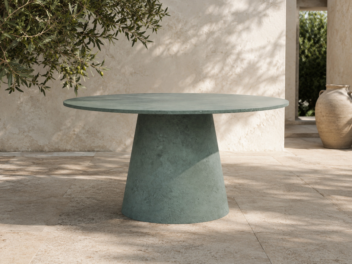 Tavolo ORBIS MANOFATTI in finitura verde salvia ambientato su una terrazza mediterranea in pietra con ombre di ulivo