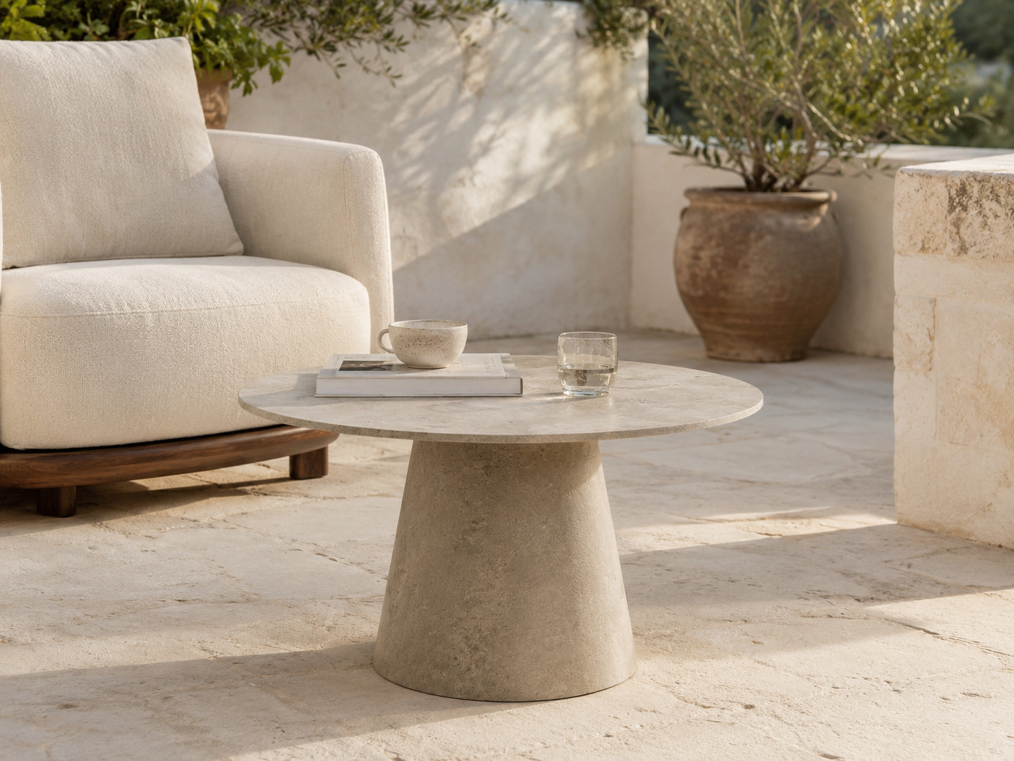 Tavolo basso ORBIS MANOFATTI in finitura sabbia ambientato in una lounge outdoor mediterranea in pietra