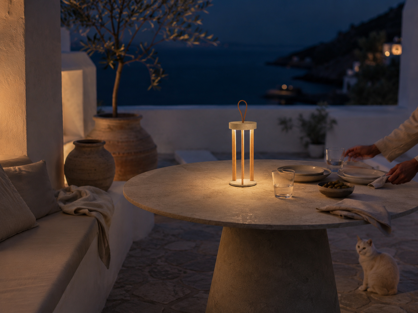 Lampada portatile TIZIA MANOFATTI in finitura sabbia accesa su tavola outdoor in terrazza mediterranea vista mare